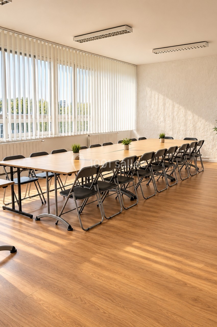 Salle de réunion lumineuse avec une longue table en bois, des chaises pliantes et des plantes décoratives.