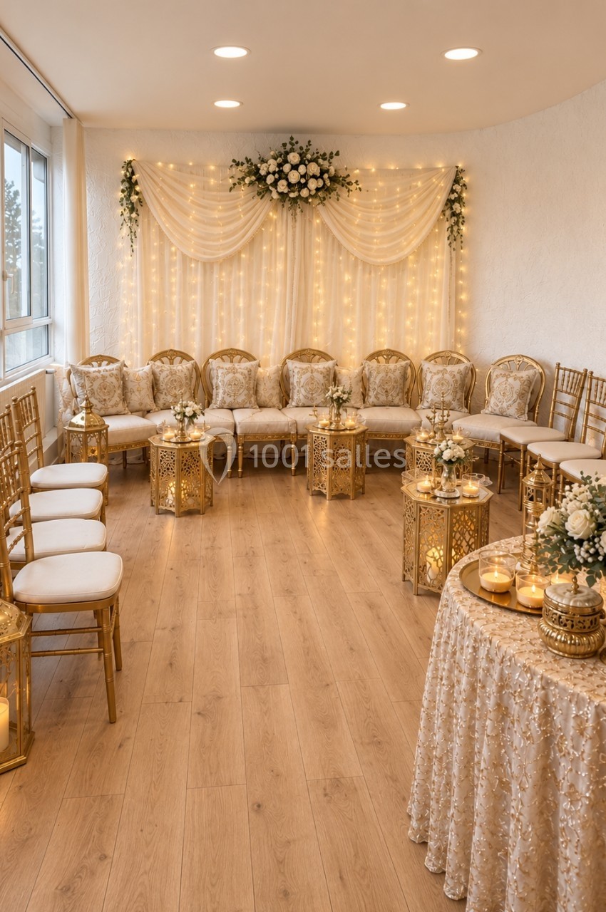 Salle décorée pour un événement, avec chaises alignées, lanternes dorées, guirlandes lumineuses et compositions florales.