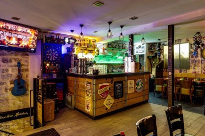 Intérieur d'un bar avec tables, chaises, murs décorés et enseigne lumineuse, ambiance chaleureuse et décontractée.