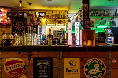 Intérieur d'un bar avec tables, chaises, murs décorés et enseigne lumineuse, ambiance chaleureuse et décontractée.