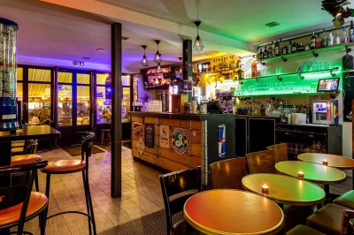 Intérieur d'un bar avec tables, chaises, murs décorés et enseigne lumineuse, ambiance chaleureuse et décontractée.