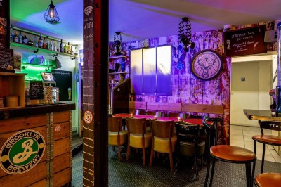 Intérieur d'un bar avec tables, chaises, murs décorés et enseigne lumineuse, ambiance chaleureuse et décontractée.
