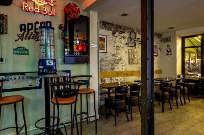 Intérieur d'un bar avec tables, chaises, murs décorés et enseigne lumineuse, ambiance chaleureuse et décontractée.