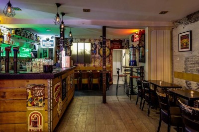 Intérieur d'un bar avec tables, chaises, murs décorés et enseigne lumineuse, ambiance chaleureuse et décontractée.
