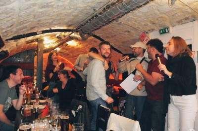 Intérieur d'un bar avec tables, chaises, murs décorés et enseigne lumineuse, ambiance chaleureuse et décontractée.