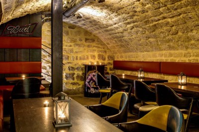 Intérieur d'un bar avec tables, chaises, murs décorés et enseigne lumineuse, ambiance chaleureuse et décontractée.