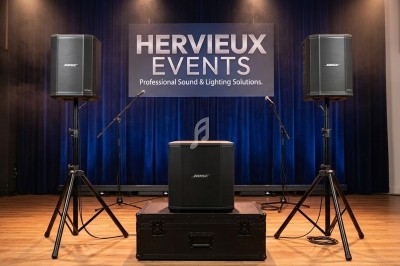 Miniature DJ Cachan (Val-de-Marne) - Hervieux Event #2 Deux enceintes sur trépieds et un caisson de basses Bose installés sur une scène avec un fond bleu et un panneau ’Hervieux…