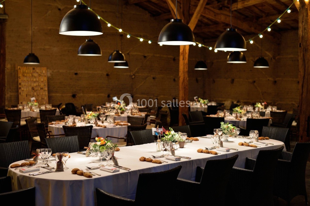 Salle de réception décorée avec des tables dressées, éclairée par des suspensions noires et des guirlandes lumineuses.