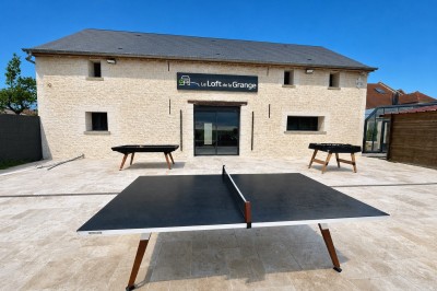 Table de ping-pong en extérieur devant un bâtiment en pierre avec une enseigne ’Le Loft de la Grange’.