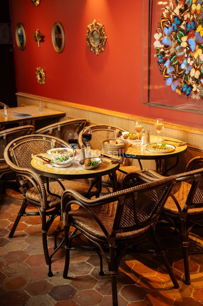 Tables en rotin avec assiettes servies, verres de vin et décoration murale colorée dans un restaurant chaleureux.