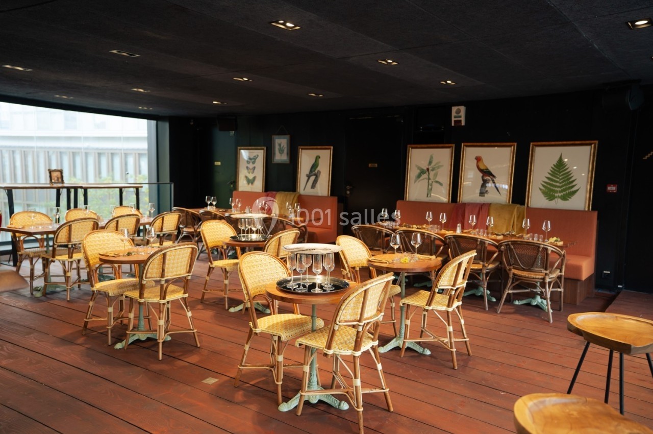 Salle de restaurant avec chaises en rotin, tables rondes et décorations murales représentant des oiseaux et des plantes.