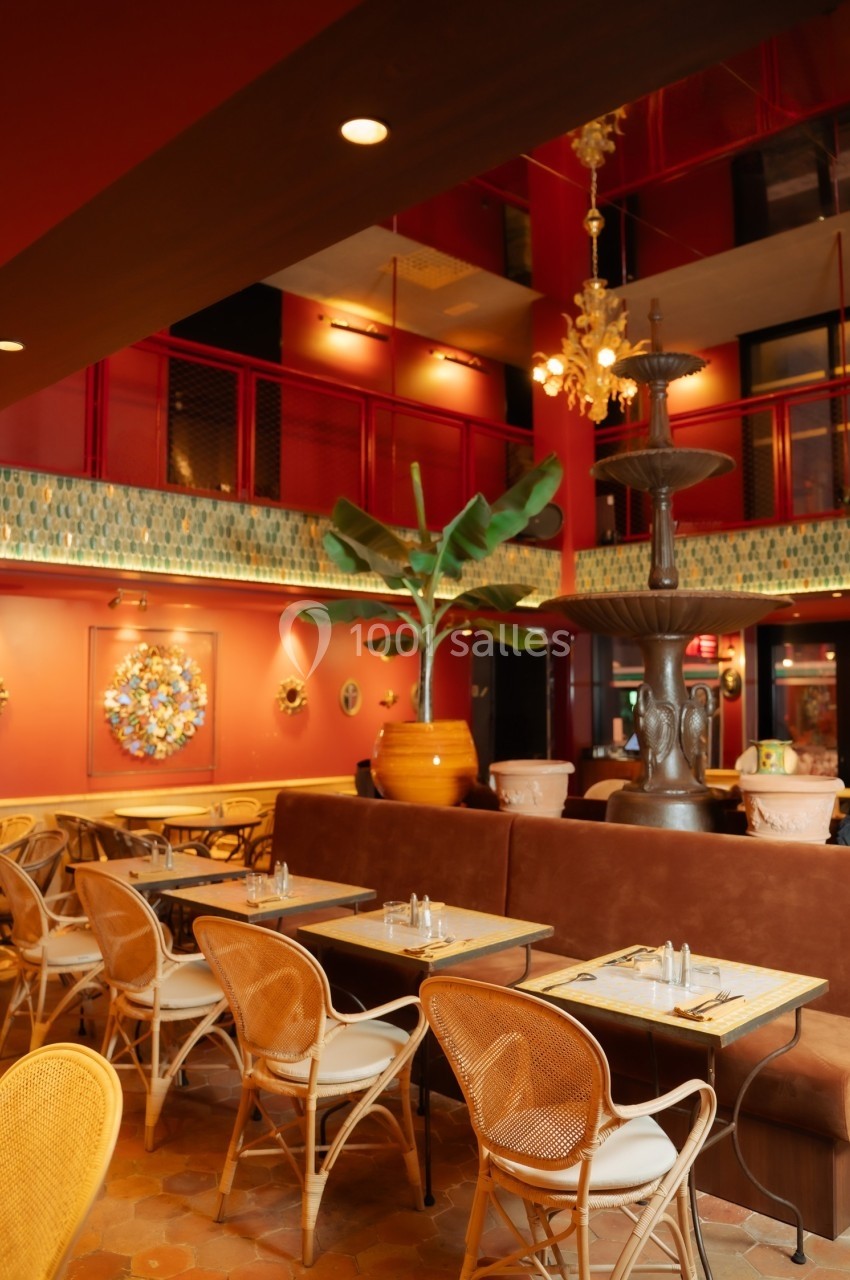Salle de restaurant chaleureuse avec murs rouges, mobilier en rotin, plantes et éclairage tamisé.