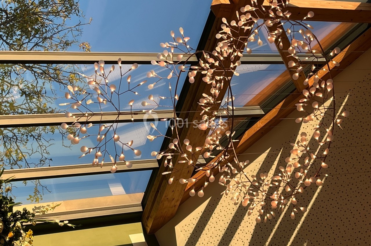 Suspension lumineuse décorative en forme de branches avec des feuilles dorées, éclairée par une verrière ensoleillée.