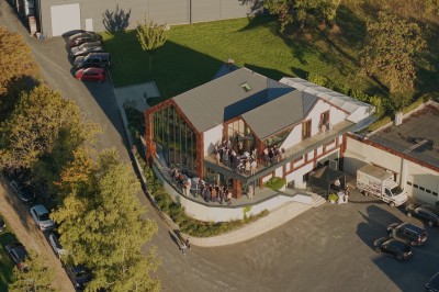 Vue aérienne d'un bâtiment moderne entouré de verdure, avec des personnes rassemblées sur une terrasse.