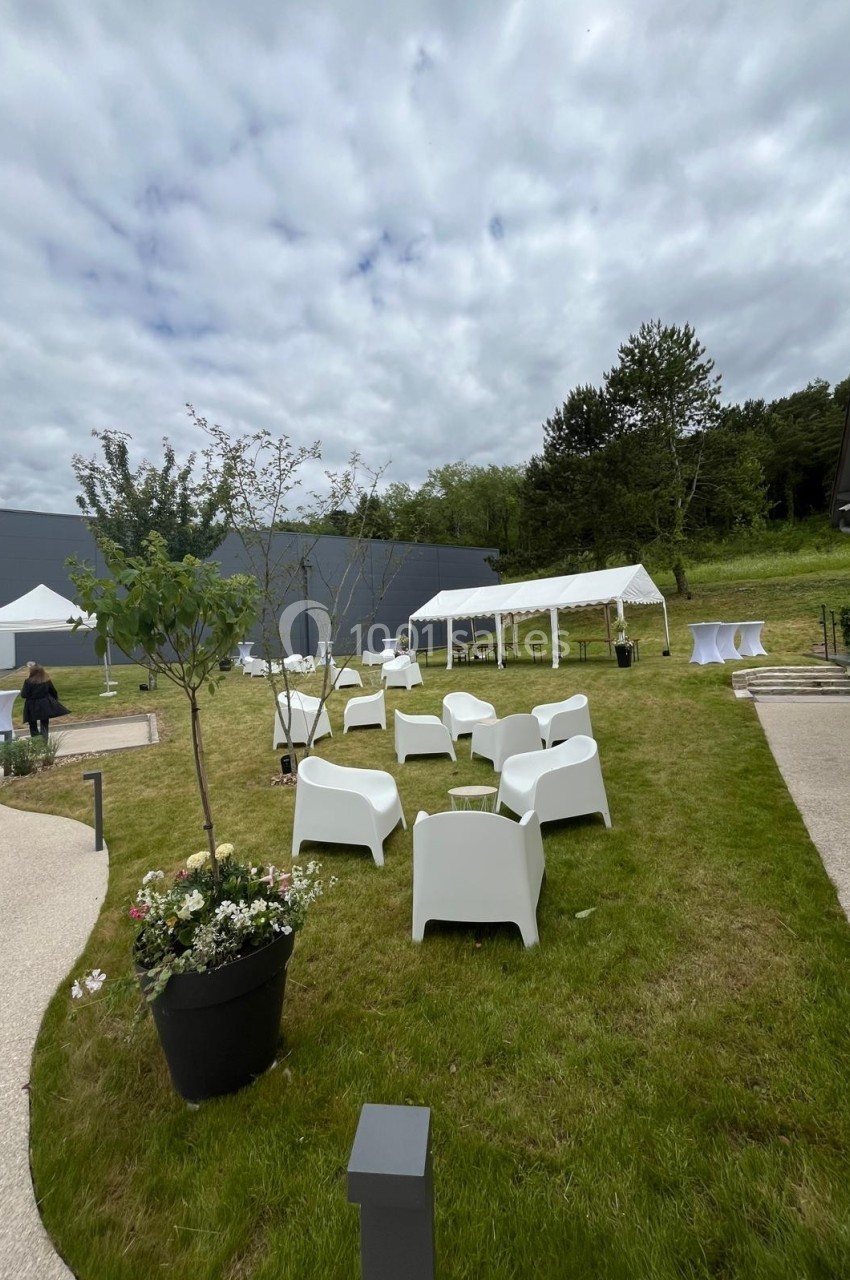 Espace extérieur aménagé avec chaises blanches, tentes et tables sur une pelouse sous un ciel nuageux.