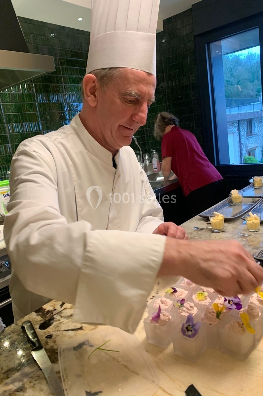 Un chef en tenue blanche décore des verrines avec des fleurs comestibles dans une cuisine moderne.