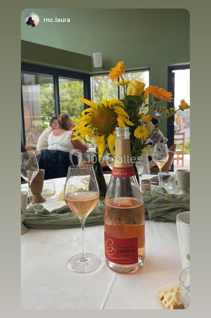 Bouteille de vin rosé et verre servis sur une table dressée avec des fleurs jaunes en arrière-plan lumineux.