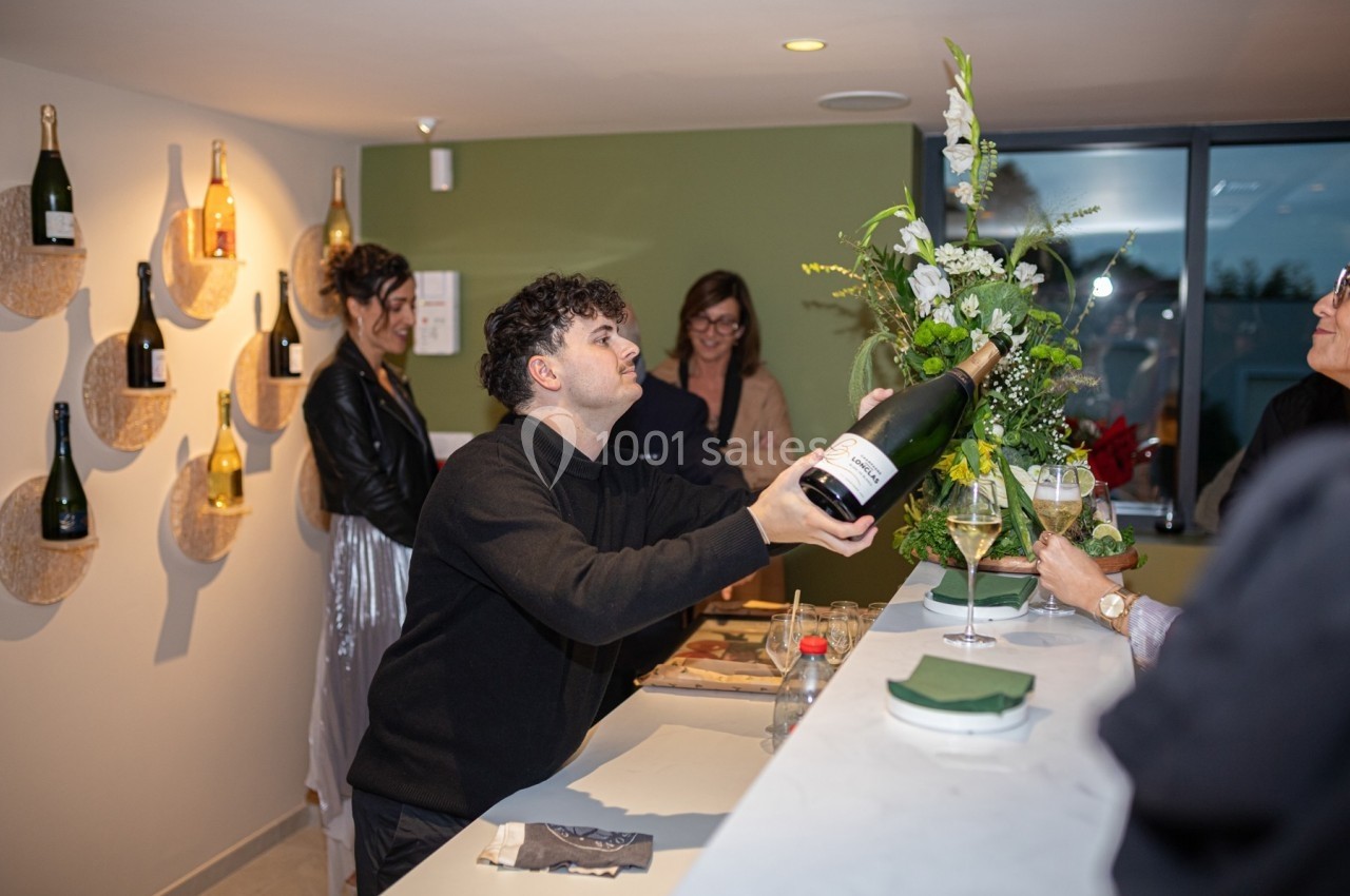 Un serveur présente une bouteille de champagne à un groupe de personnes dans un espace moderne et convivial.