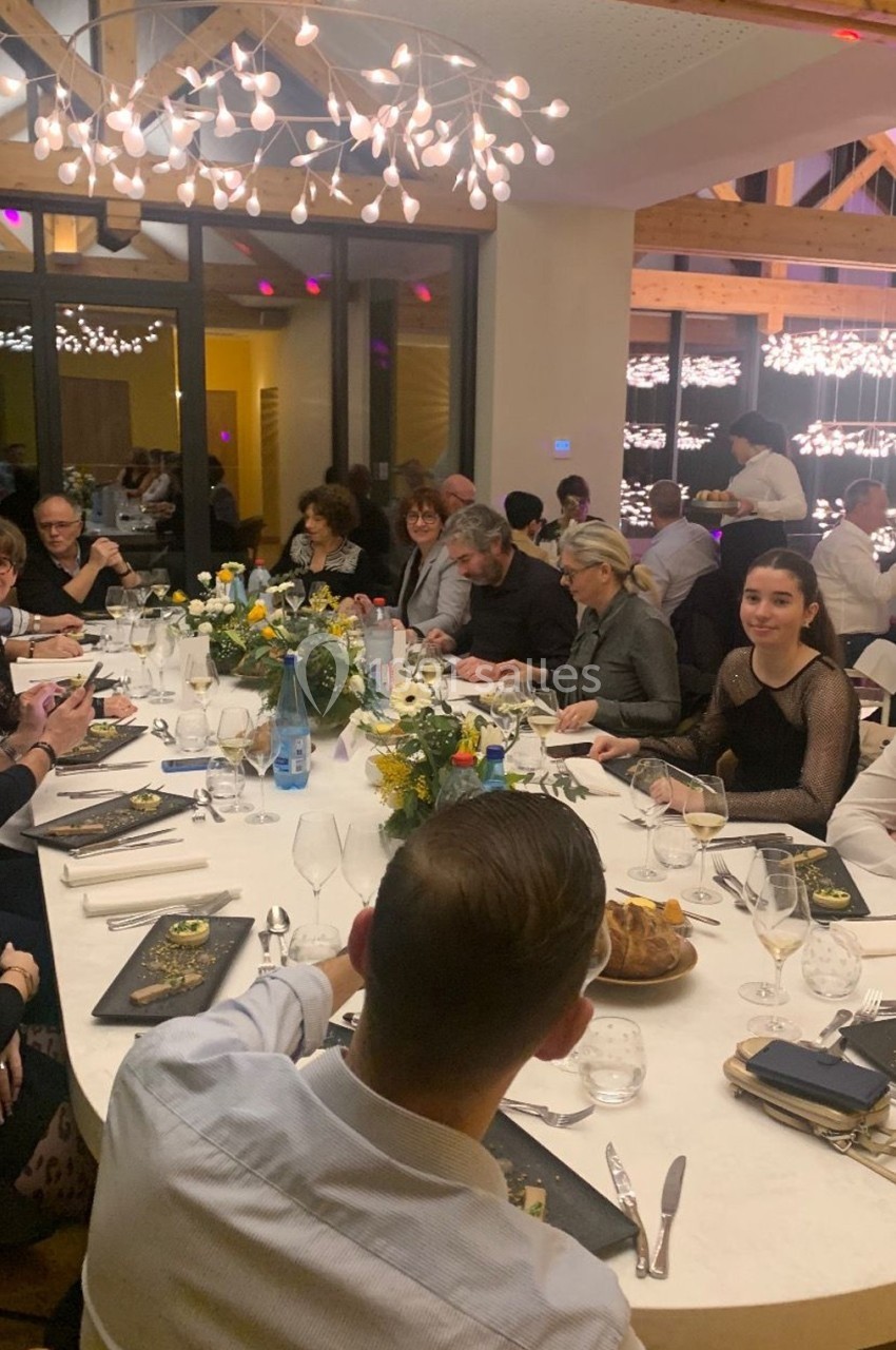 Des convives assis autour d'une grande table ronde décorée de fleurs, lors d'un dîner dans une salle lumineuse.