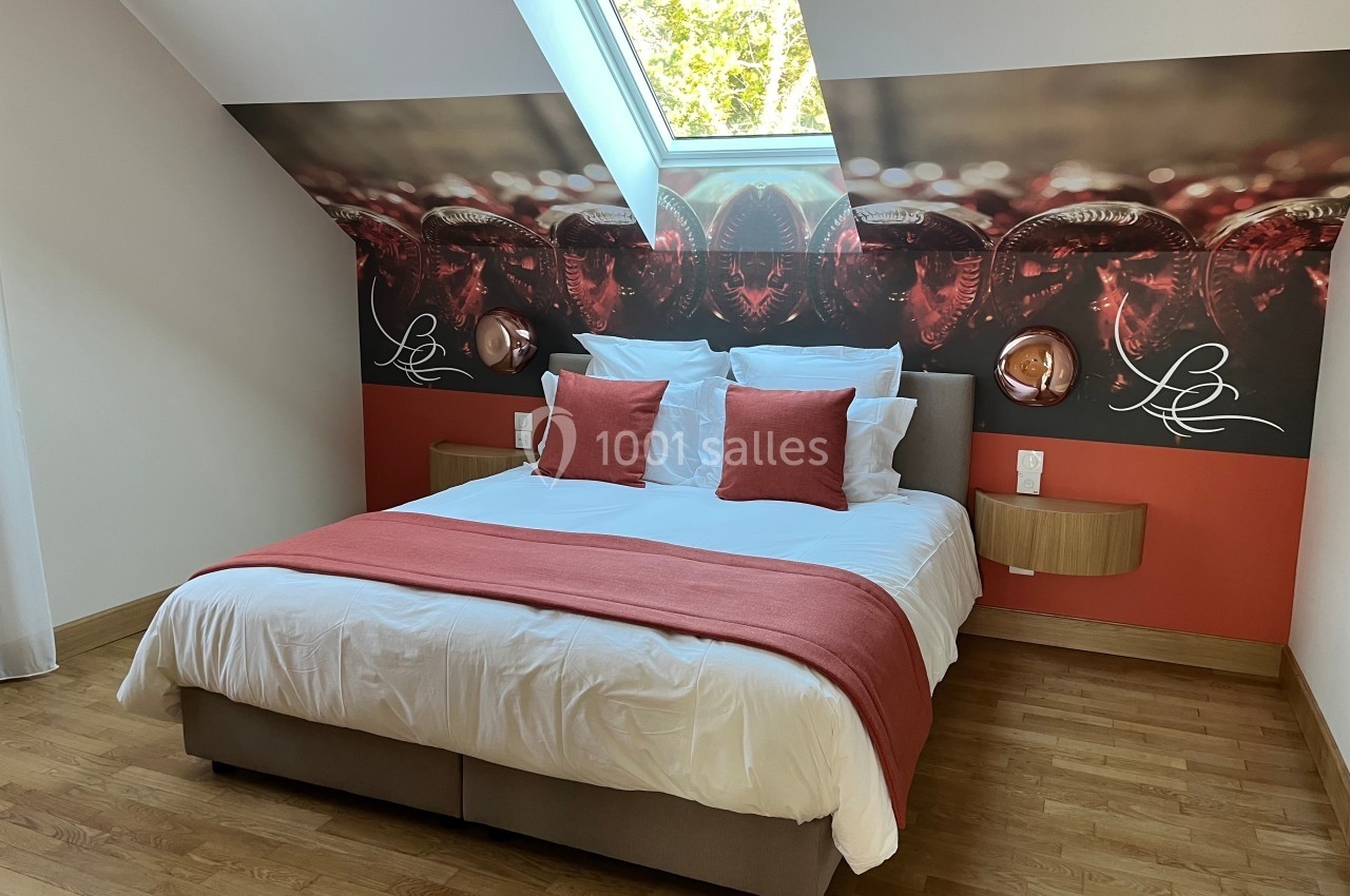 Lit double avec draps blancs, coussins et jeté rouges, sous un puits de lumière dans une chambre au décor moderne.