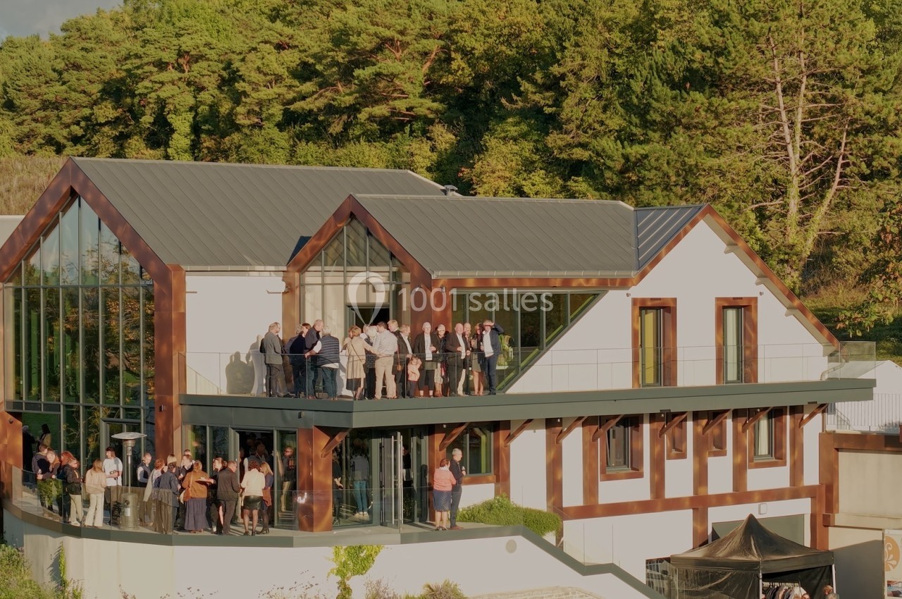 Groupe de personnes rassemblées sur la terrasse et devant un bâtiment moderne entouré de végétation.
