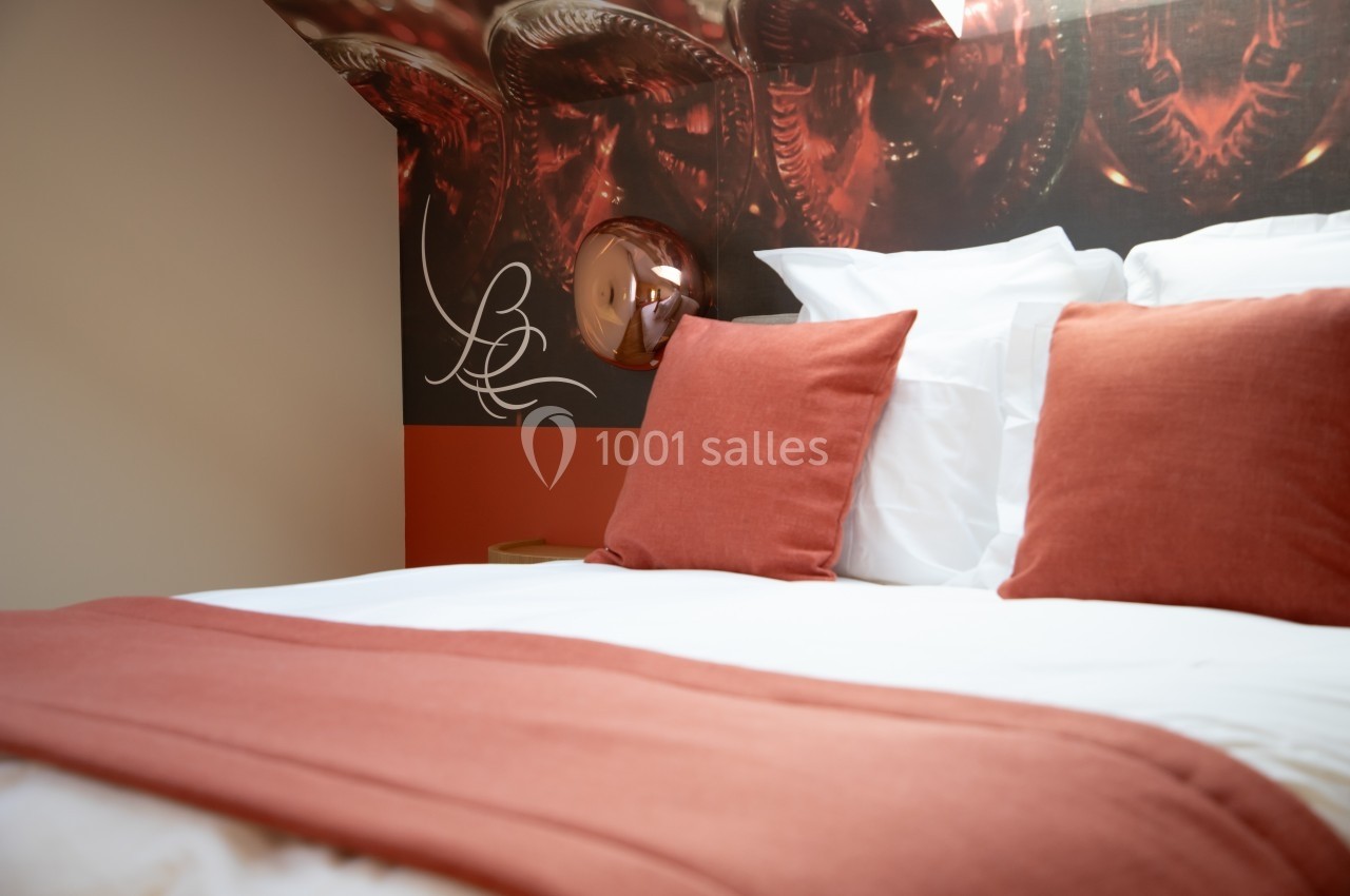 Lit double avec draps blancs, coussins et plaid rouges, dans une chambre décorée de tons chauds et motifs modernes.
