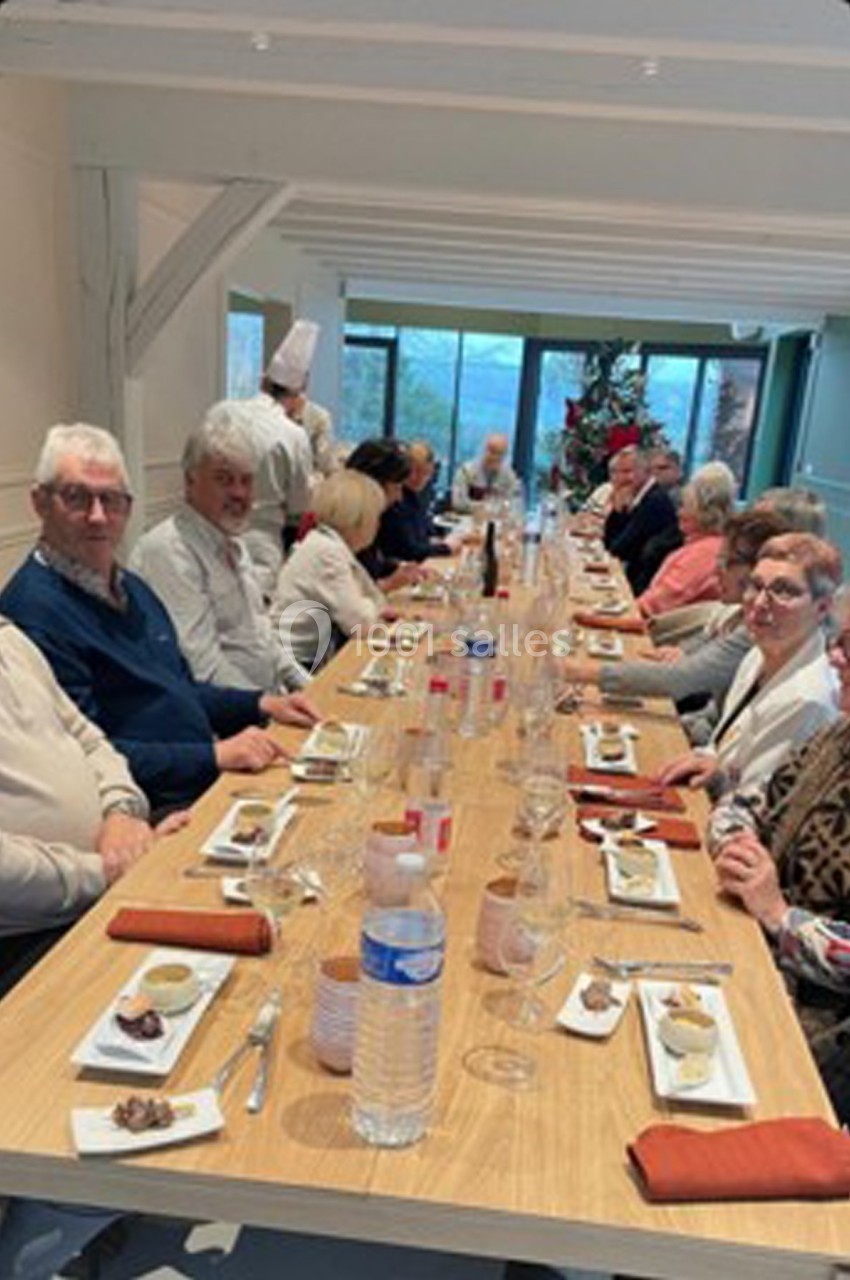 Des personnes assises autour d'une longue table dressée, partageant un repas dans une salle lumineuse.