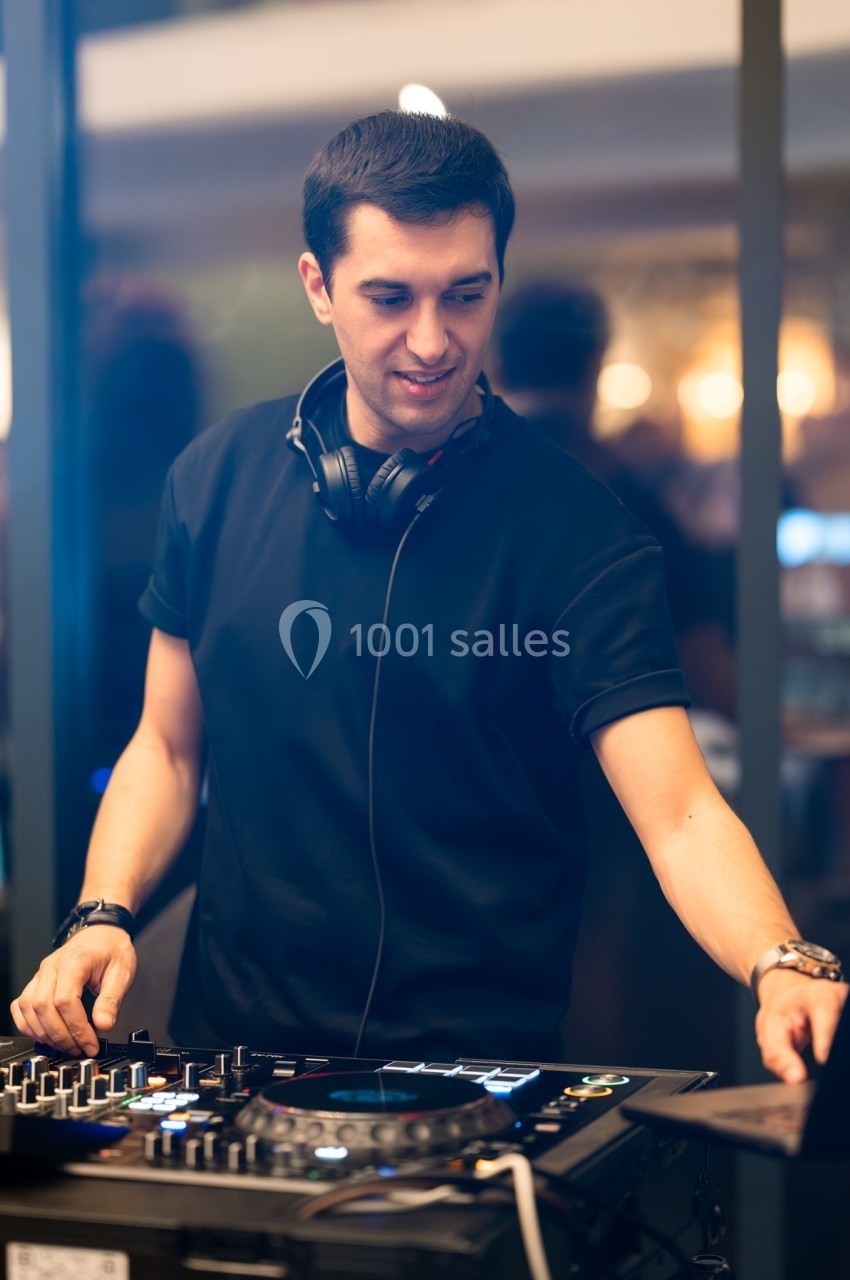 Un DJ mixe de la musique sur une table de mixage dans un environnement intérieur lumineux.