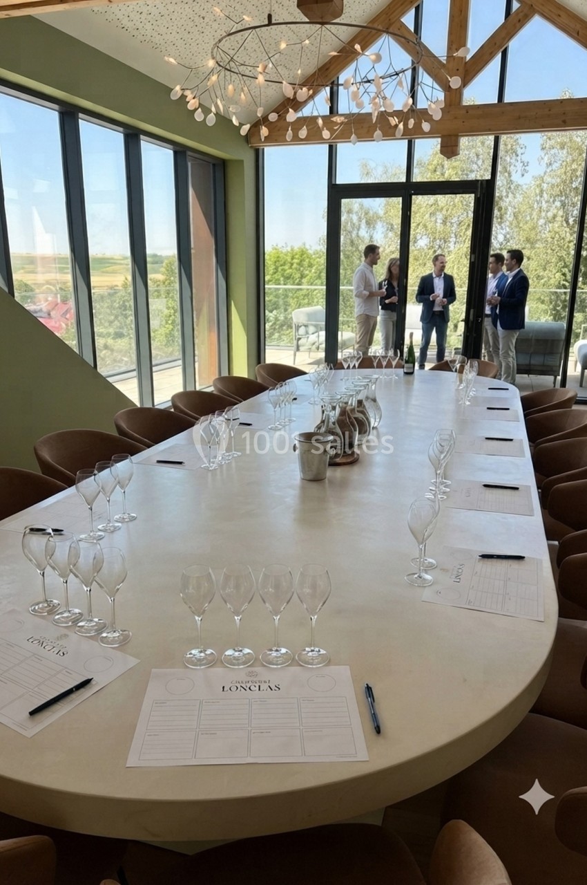 Grande table ovale dressée avec des verres et des documents, dans une salle lumineuse avec vue sur un paysage verdoyant.