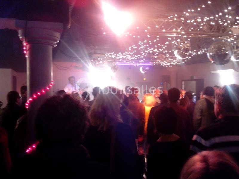 Foule rassemblée dans une salle décorée de guirlandes lumineuses, avec un musicien sur une scène éclairée.