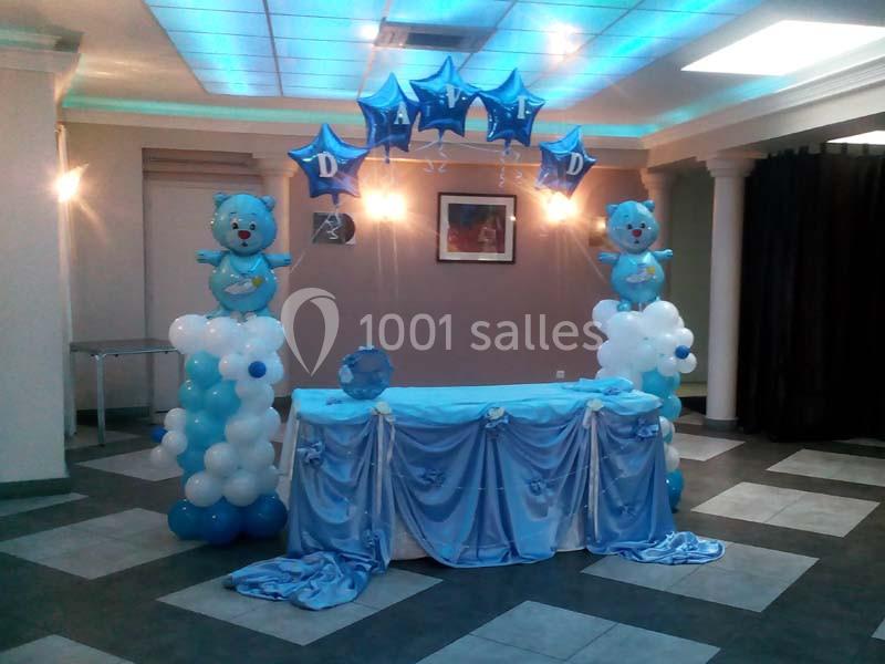 Décoration de fête avec ballons bleus en forme d'ours et d'étoiles, table drapée de tissu bleu dans une salle éclairée.