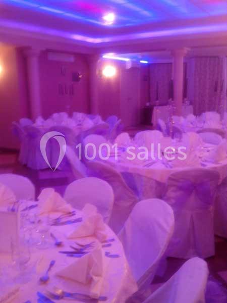Salle de réception décorée avec des tables rondes, nappes blanches et éclairage d'ambiance violet.