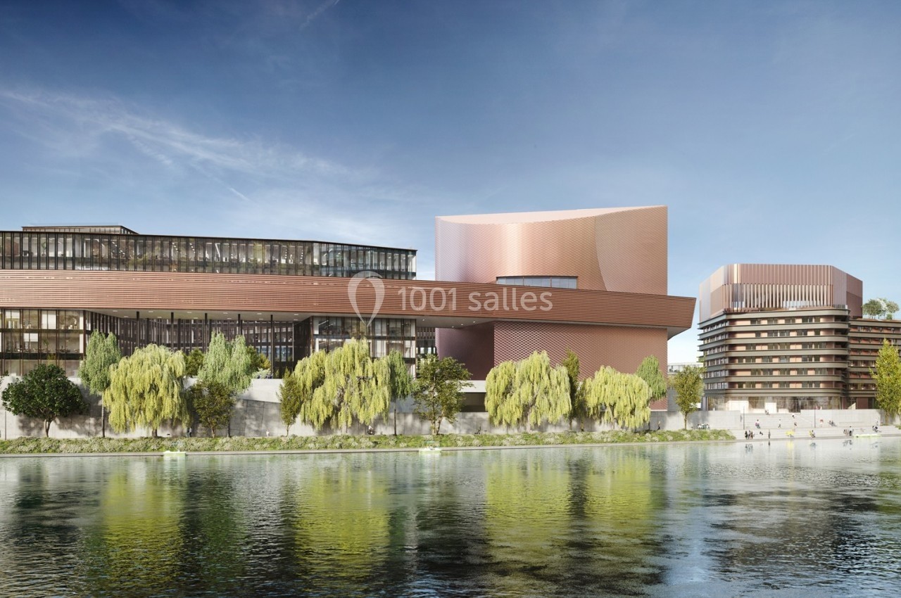Vue d'un complexe architectural moderne en bord de rivière, entouré d'arbres et reflété dans l'eau calme.