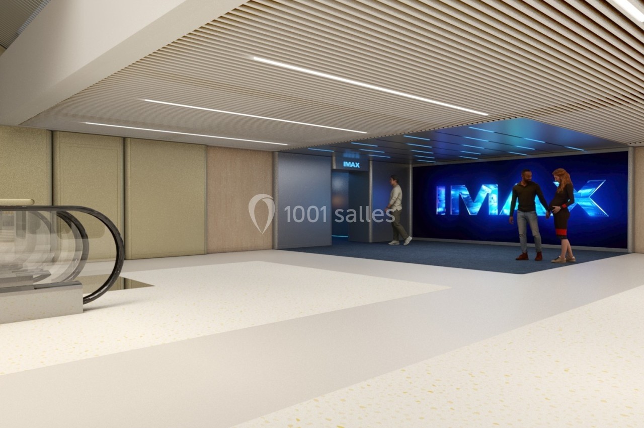 Entrée d'une salle IMAX avec un sol clair, un escalator à gauche et des personnes discutant près de l'entrée.