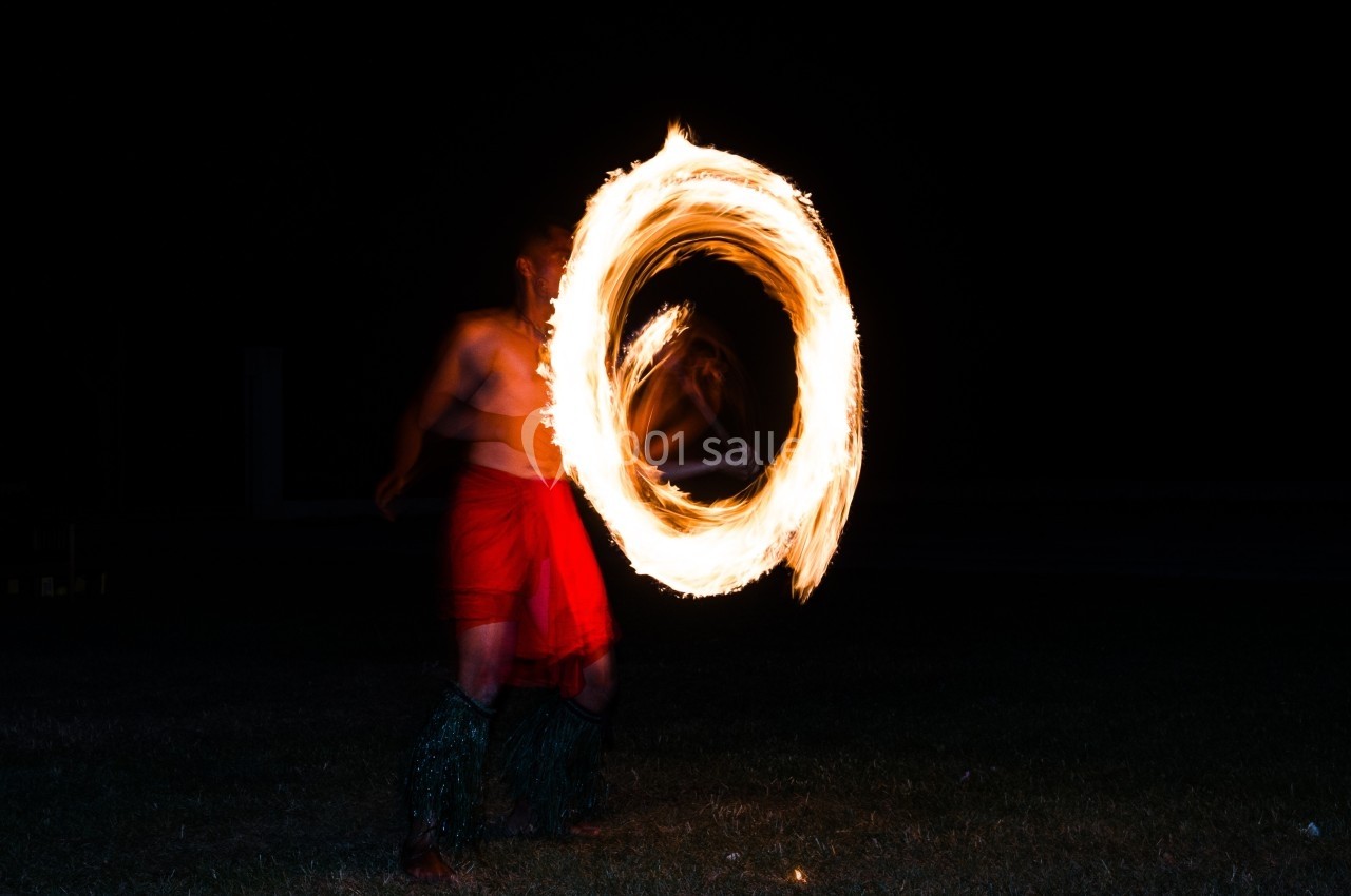 Un danseur de feu en mouvement, créant un cercle lumineux avec une torche enflammée dans l'obscurité.