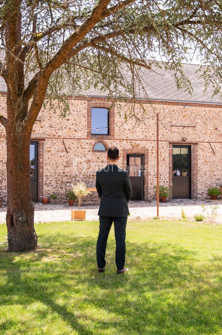 Un homme en costume debout sur une pelouse regarde un bâtiment en pierre avec des portes et fenêtres.