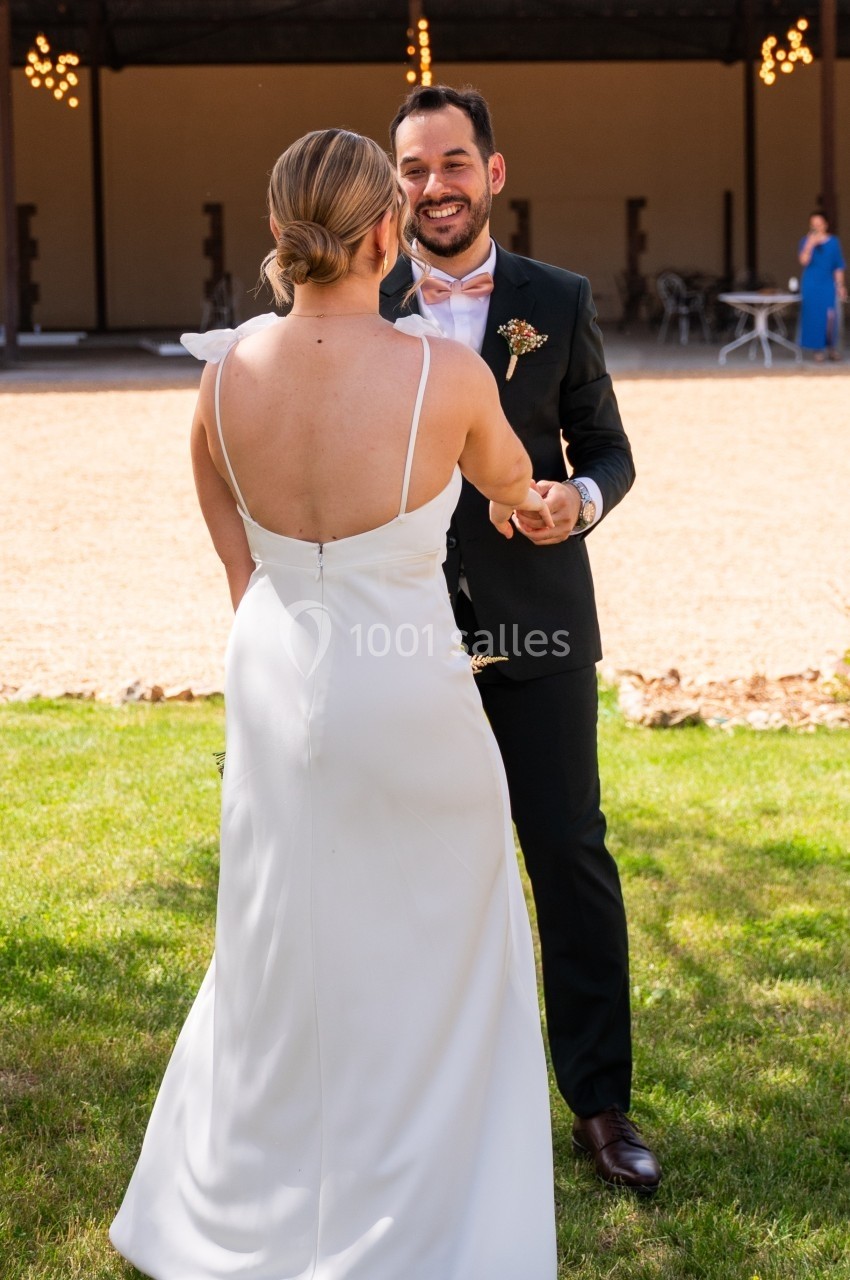 Un couple en tenue de mariage danse sur une pelouse devant un bâtiment ouvert.