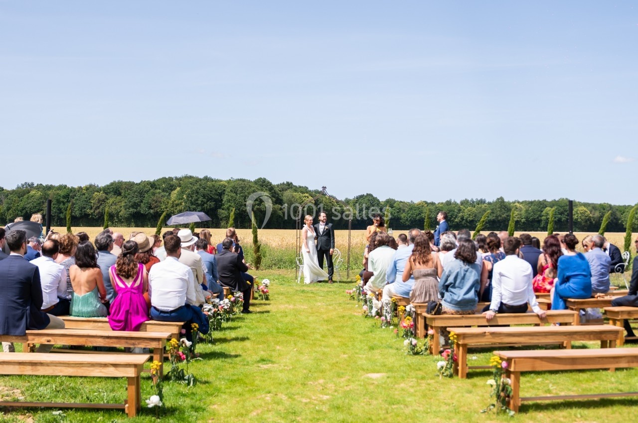 Cérémonie de mariage en plein air avec des invités assis sur des bancs, face aux mariés et à l'officiant.