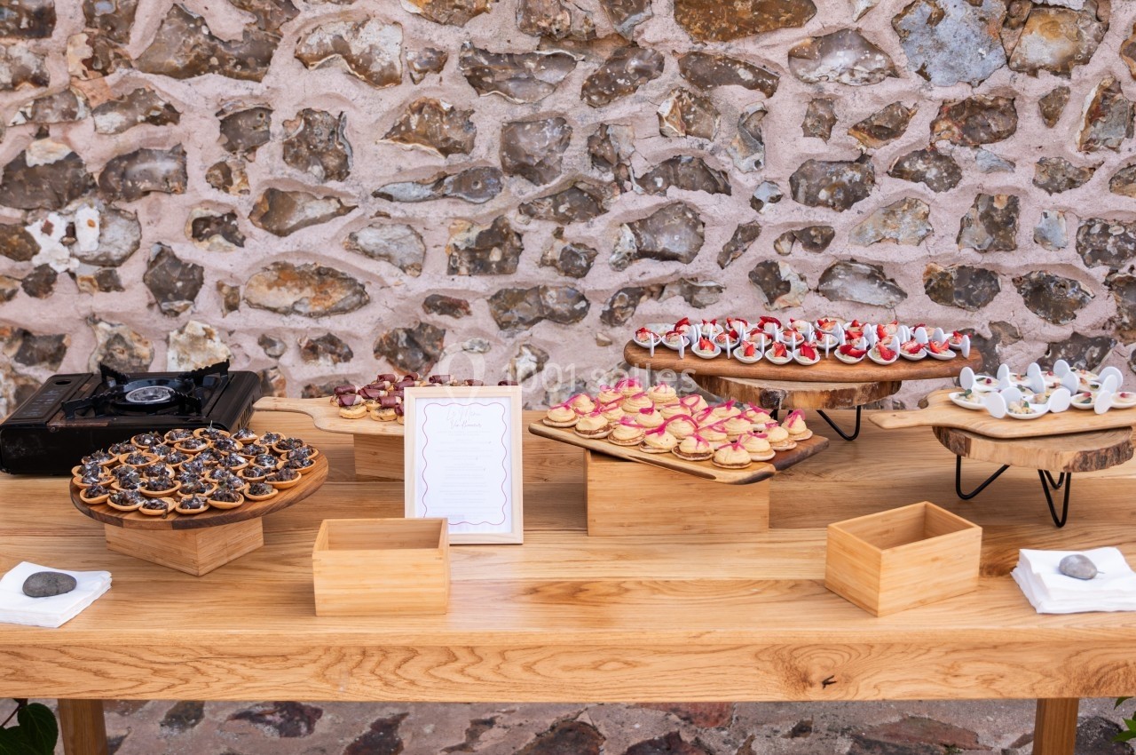 Table en bois avec des plateaux de bouchées apéritives variées devant un mur en pierre.