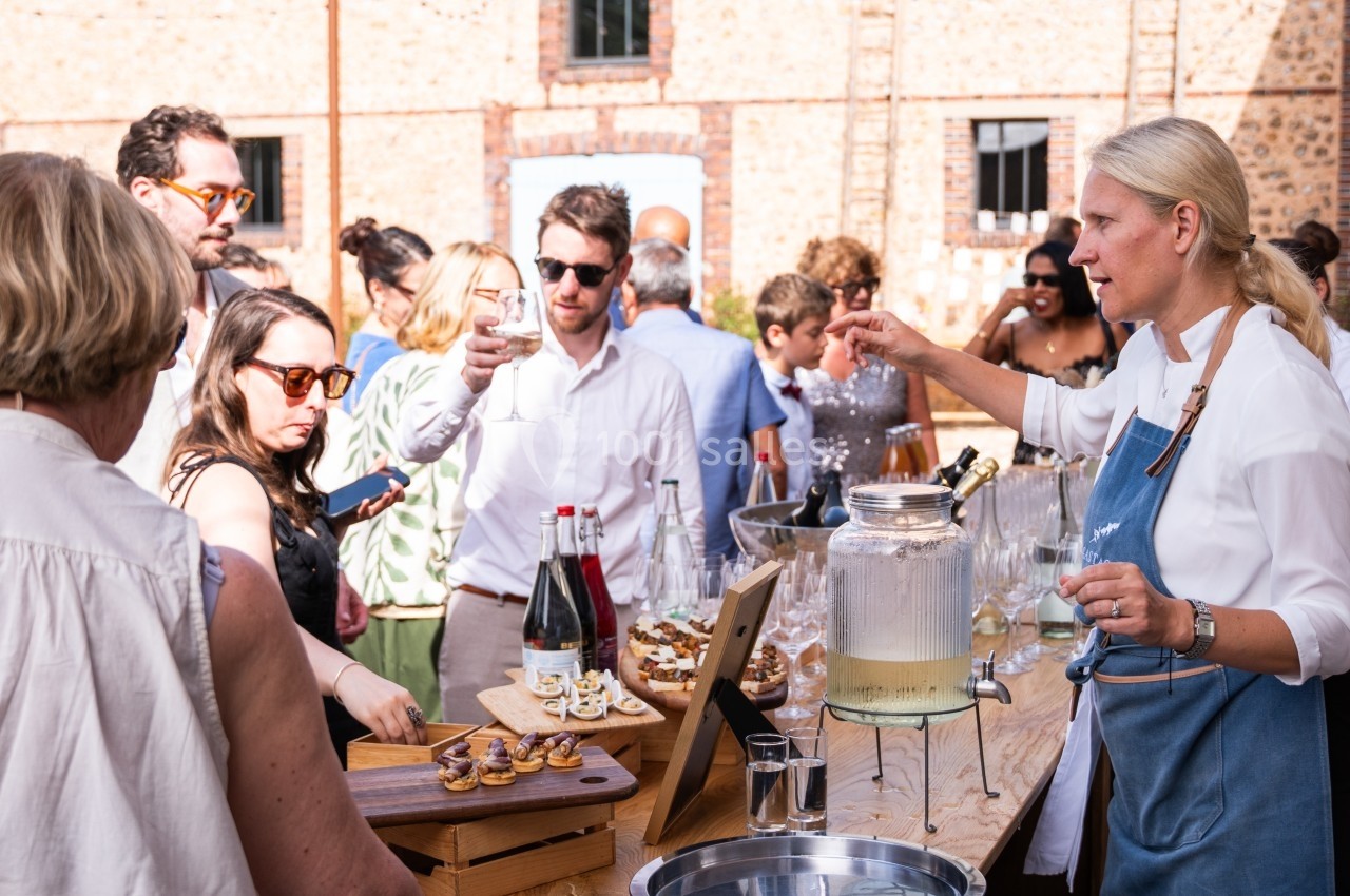 Personnes rassemblées autour d'une table en extérieur, dégustant des boissons et des amuse-bouches lors d'un événement.
