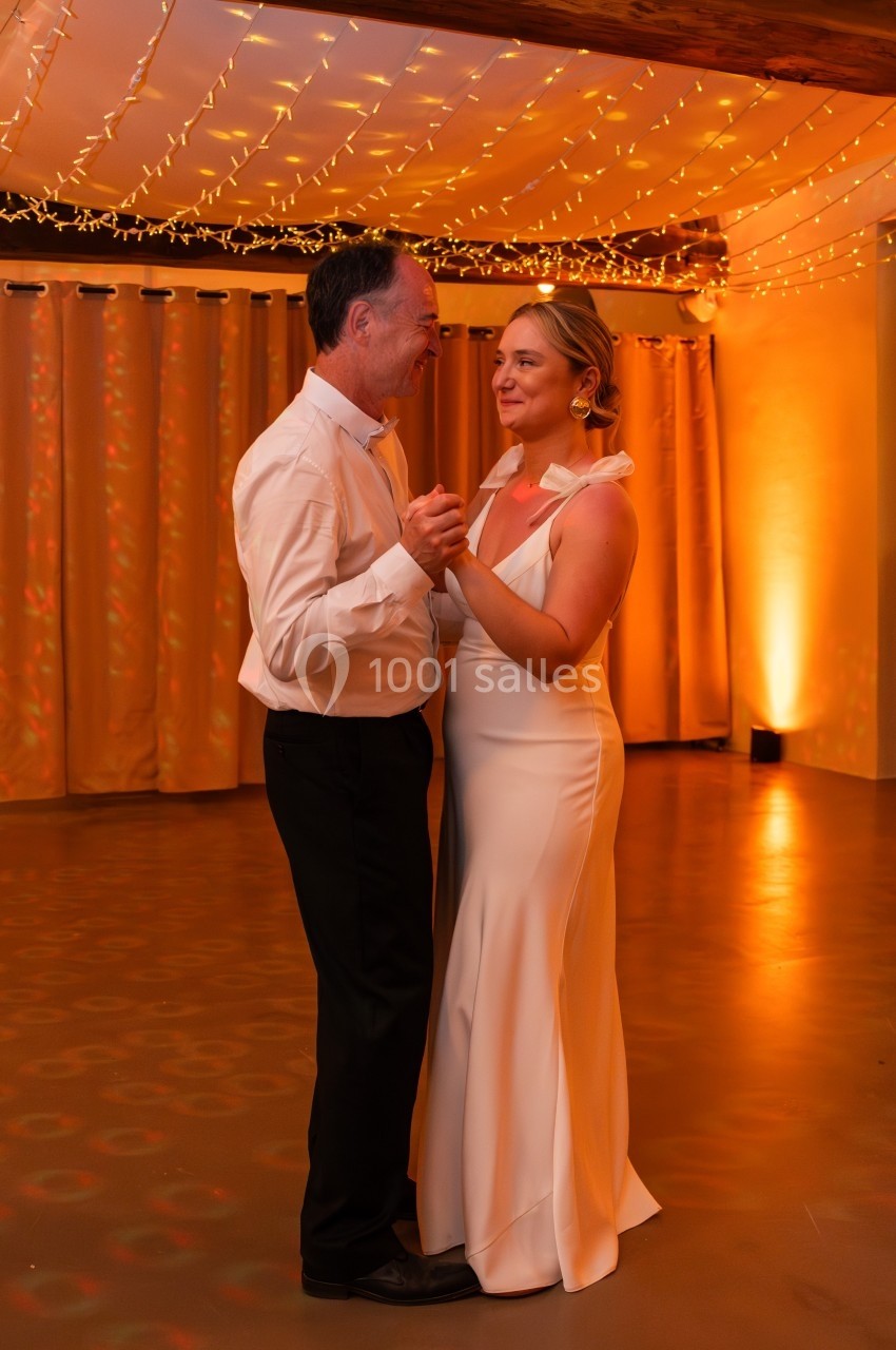 Un couple danse ensemble dans une salle éclairée par des guirlandes lumineuses et une lumière chaude.