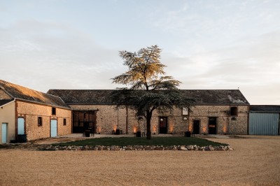 Cour extérieure d'une bâtisse en pierre avec guirlandes lumineuses suspendues et tables hautes disposées.