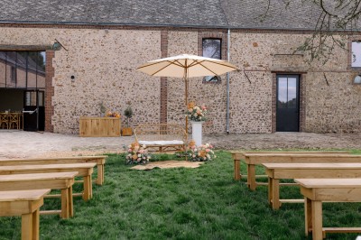 Cour extérieure d'une bâtisse en pierre avec guirlandes lumineuses suspendues et tables hautes disposées.