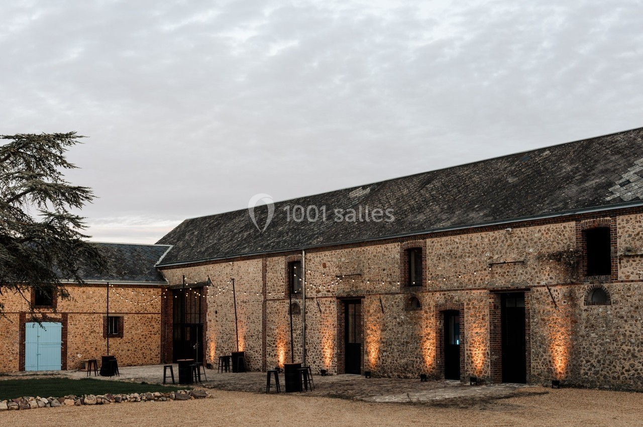 Bâtiment en pierre avec toit en ardoise, éclairé par des guirlandes lumineuses sous un ciel nuageux.