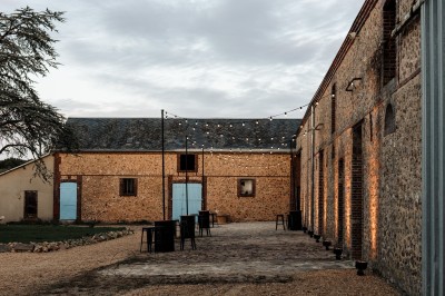 Cour extérieure d'une bâtisse en pierre avec guirlandes lumineuses suspendues et tables hautes disposées.