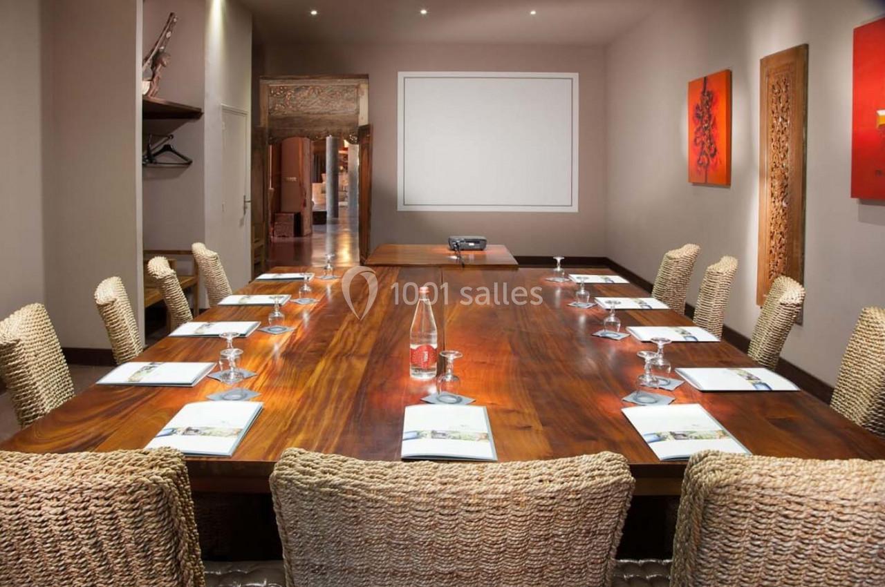 Salle de réunion avec une grande table en bois, chaises tressées, projecteur et documents disposés pour une présentation.