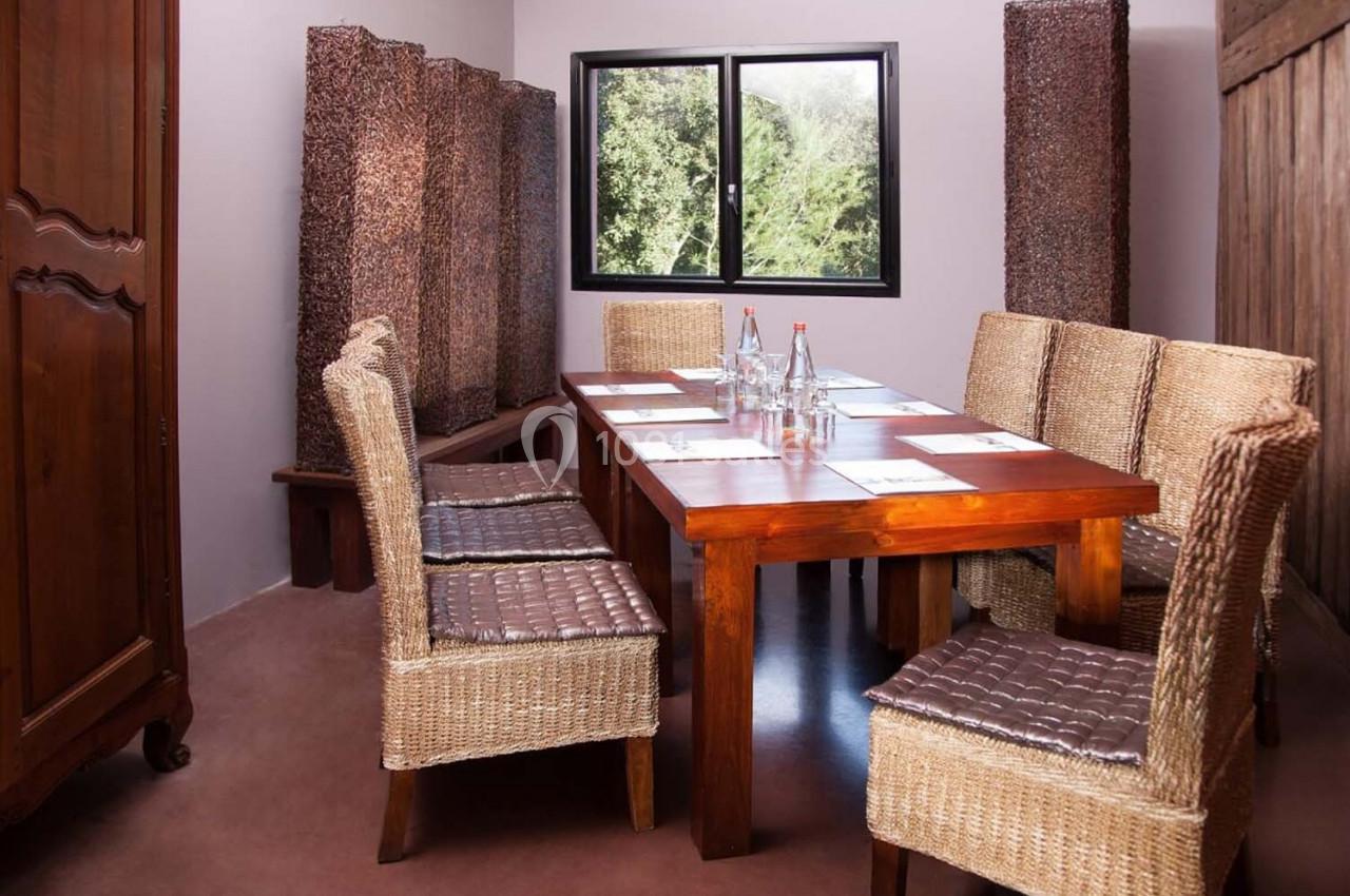 Salle de réunion avec table en bois, chaises en osier, bouteilles d'eau et fenêtre donnant sur un paysage verdoyant.
