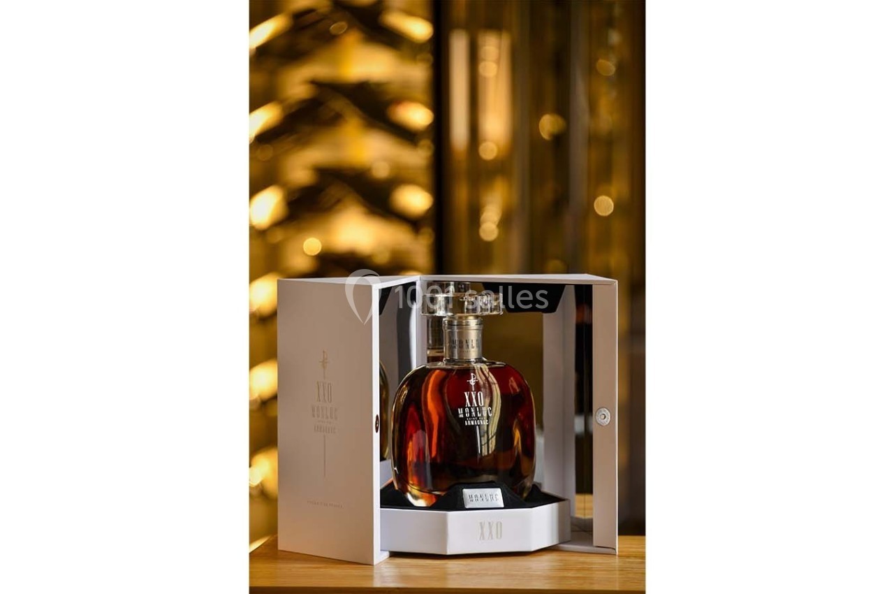 Bouteille de cognac XO présentée dans un coffret ouvert, posée sur une table avec un fond flou de cave à vin.