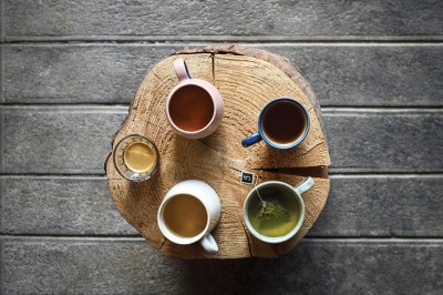 Miniature Le Club des Marques #2 Quatre boissons chaudes variées servies dans des tasses colorées, disposées sur une table en bois rond.