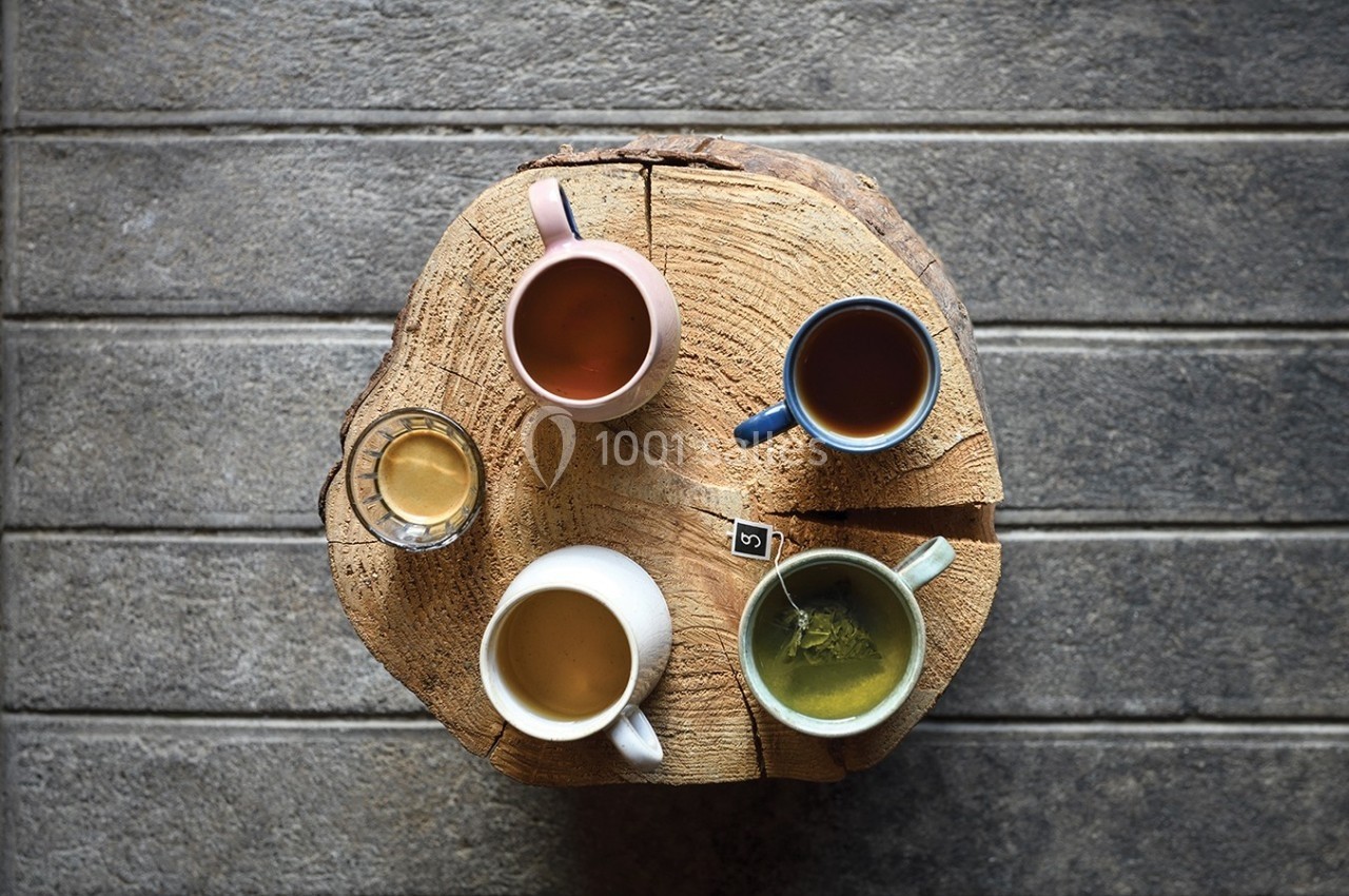 Quatre boissons chaudes variées servies dans des tasses colorées, disposées sur une table en bois rond.